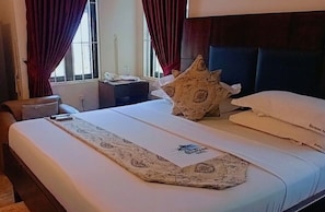 A hotel room with a bed, a nightstand, a lamp, and a window with curtains. - Monsoon Hotel Ltd (Kumasi)