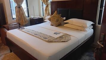 A hotel room with a bed, a bedside table with a telephone, a decorative pillow, and a window with curtains.
