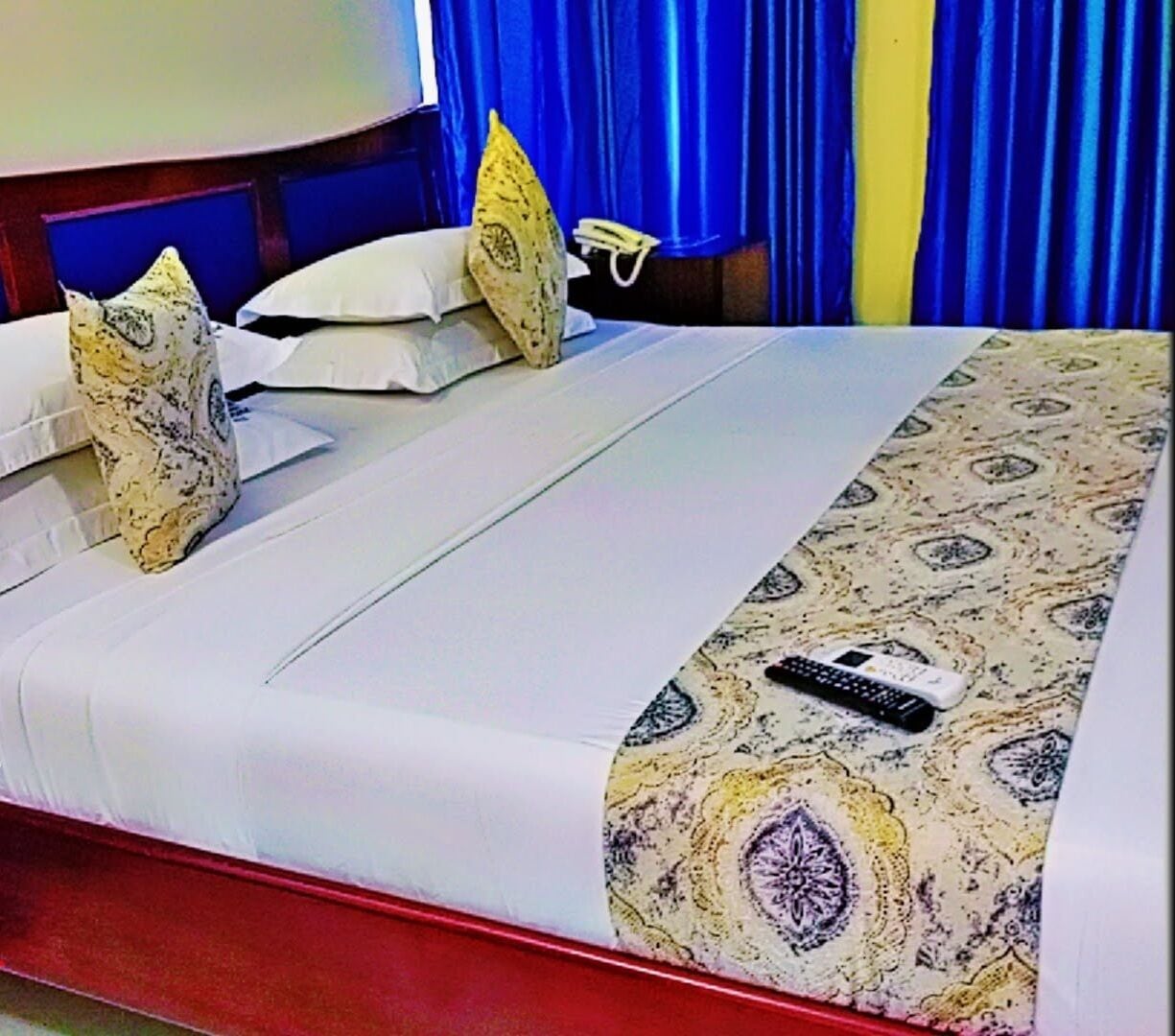 Een hotelkamer met een bed, kussens, een deken en een afstandsbediening.