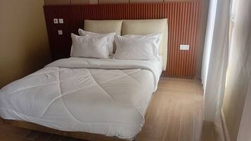 A bed with a quilted white duvet, a wooden headboard, and a wooden floor.