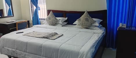 Una habitación de hotel con cama, almohadas, mesita de noche, espejo y cortinas.