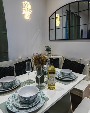A dining table set with plates, glasses, and a bottle, surrounded by black cushioned chairs. - Shrubberies Suite (Derby)
