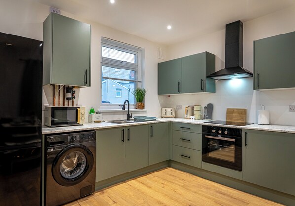 A modern kitchen with a washing machine, microwave, toaster, and oven. - Shrubberies Suite (Derby)