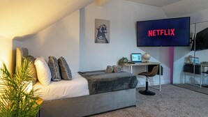 Een moderne slaapkamer met een bed, een bureau, een stoel, een televisie waarop 'NETFLIX' staat en een lijst aan de muur.
