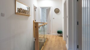 Een hal met een houten trap, een spiegel met 'HOME' erop, een klok aan de muur en een groene kruk.