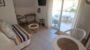Una sala de estar con un sofá, una mesita redonda, un televisor y un ventanal corredizo que da a un espacio exterior.