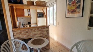 Cocina compacta con protector contra salpicaduras de ladrillo, armarios blancos y una zona de comedor con dos sillas blancas y una mesa redonda pequeña.