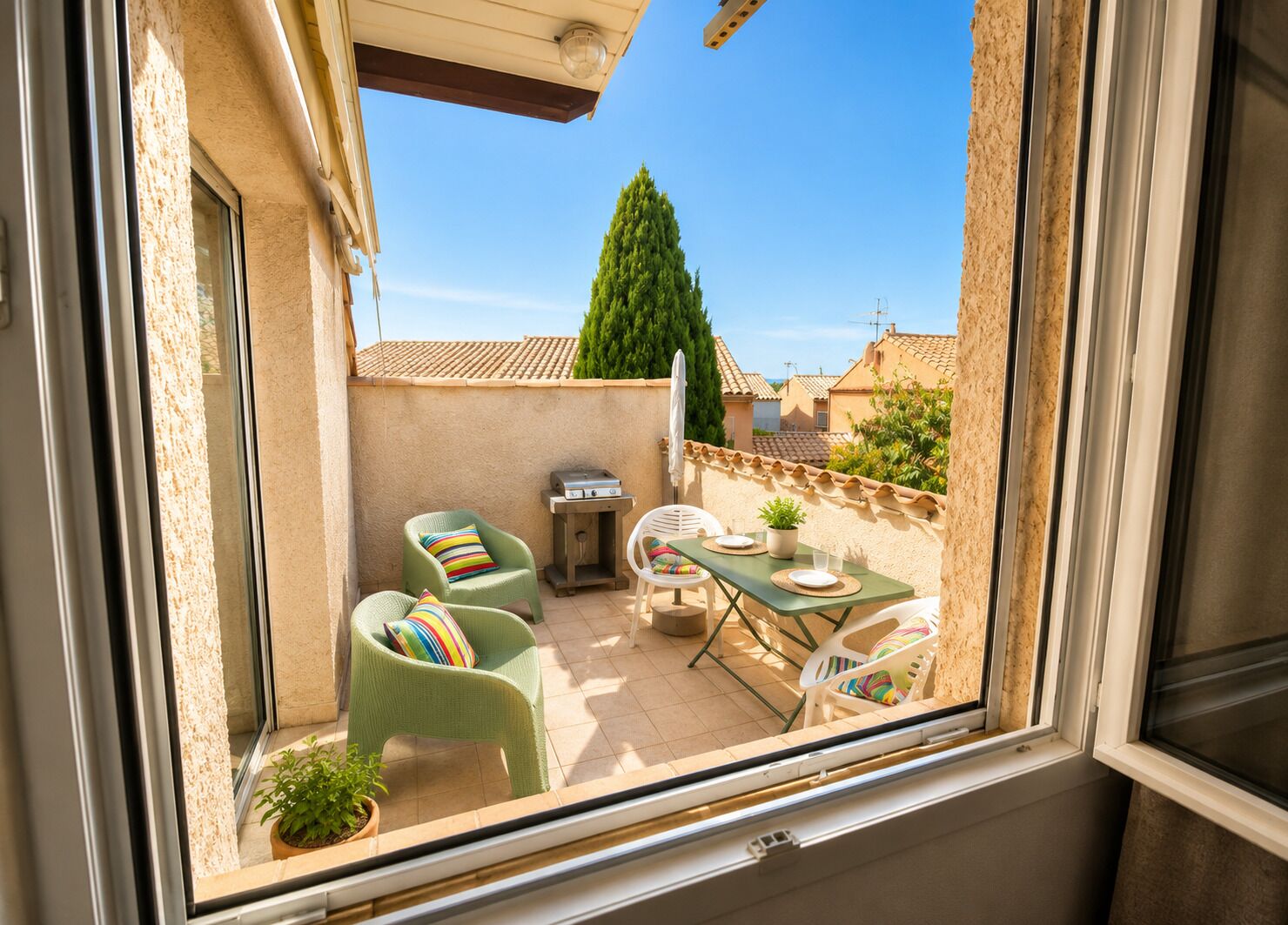 A balcony with a table, chairs, a grill, and a potted plant.