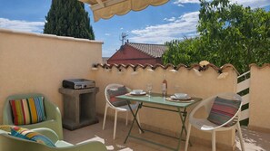 An outdoor patio with a table set for two, chairs, a small table with a radio, and a view of a house with a tiled roof. - A getaway for two between the sea and the Thau. Air conditioning, Wi-Fi, private parking. (Marseillan)