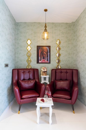Una habitación con dos sillones de cuero, una pequeña mesa blanca con un florero y copas de vino, y una lámpara colgante.