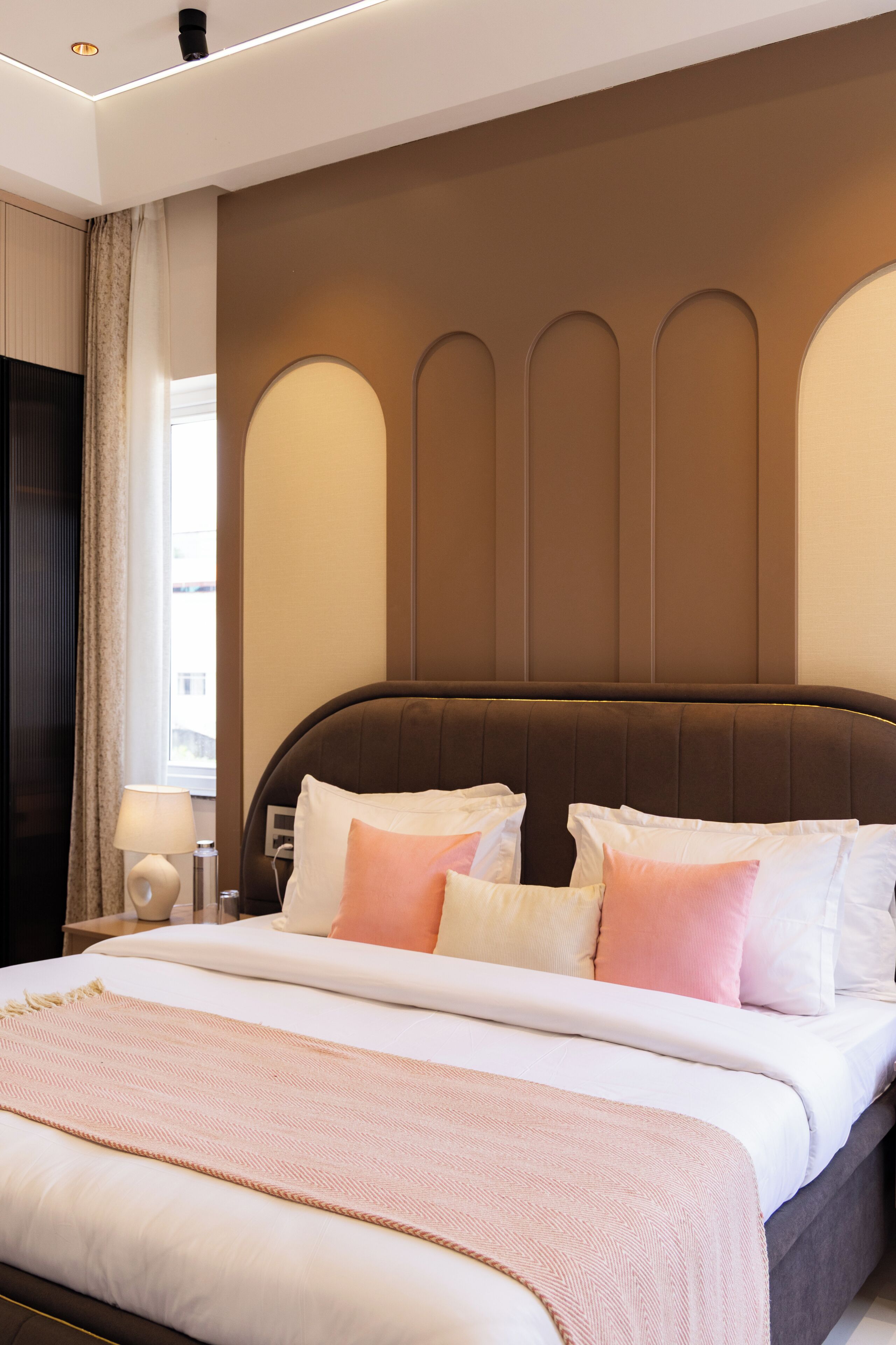 Ein Hotelzimmer mit einem großen Bett, einem Nachttisch mit Lampe und einem Fenster mit Vorhängen.