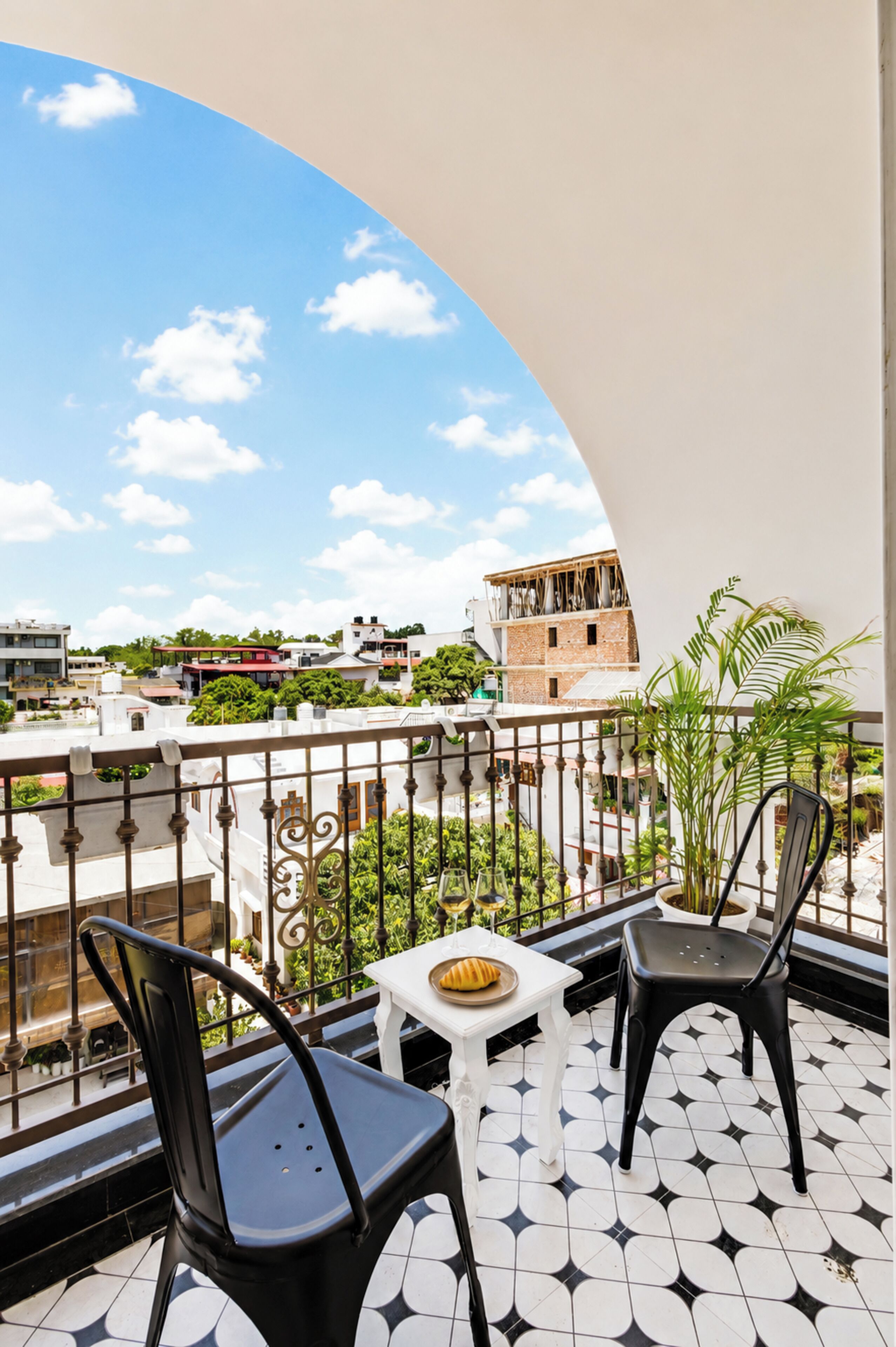A balcony with two chairs and a small table, a tiled floor, and a view of buildings and greenery.