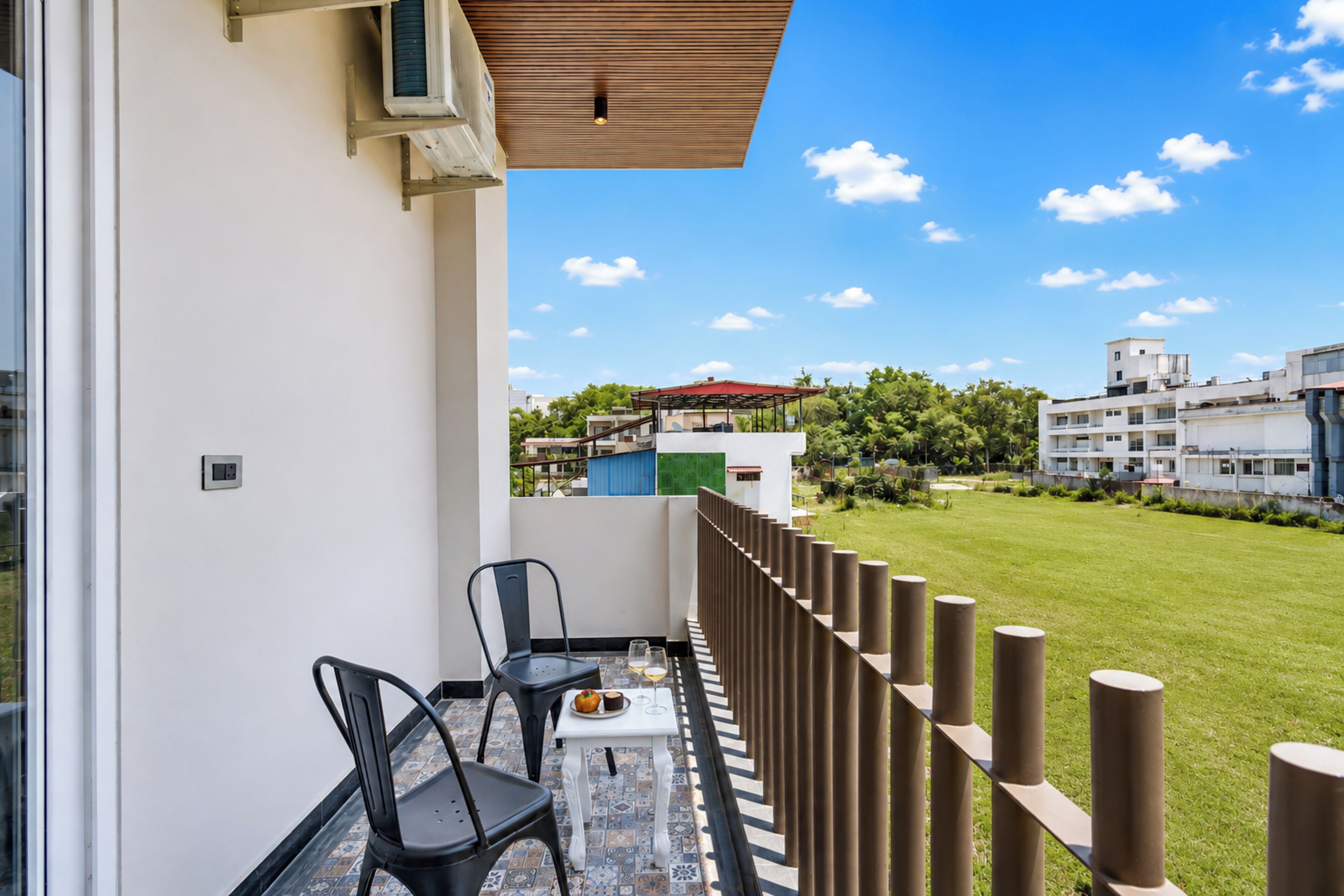 A balcony with a table, chairs, and a view of a green lawn and buildings.