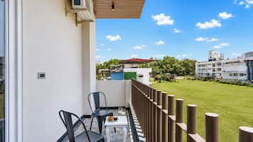A balcony with a table, chairs, and a view of a green lawn and buildings.
