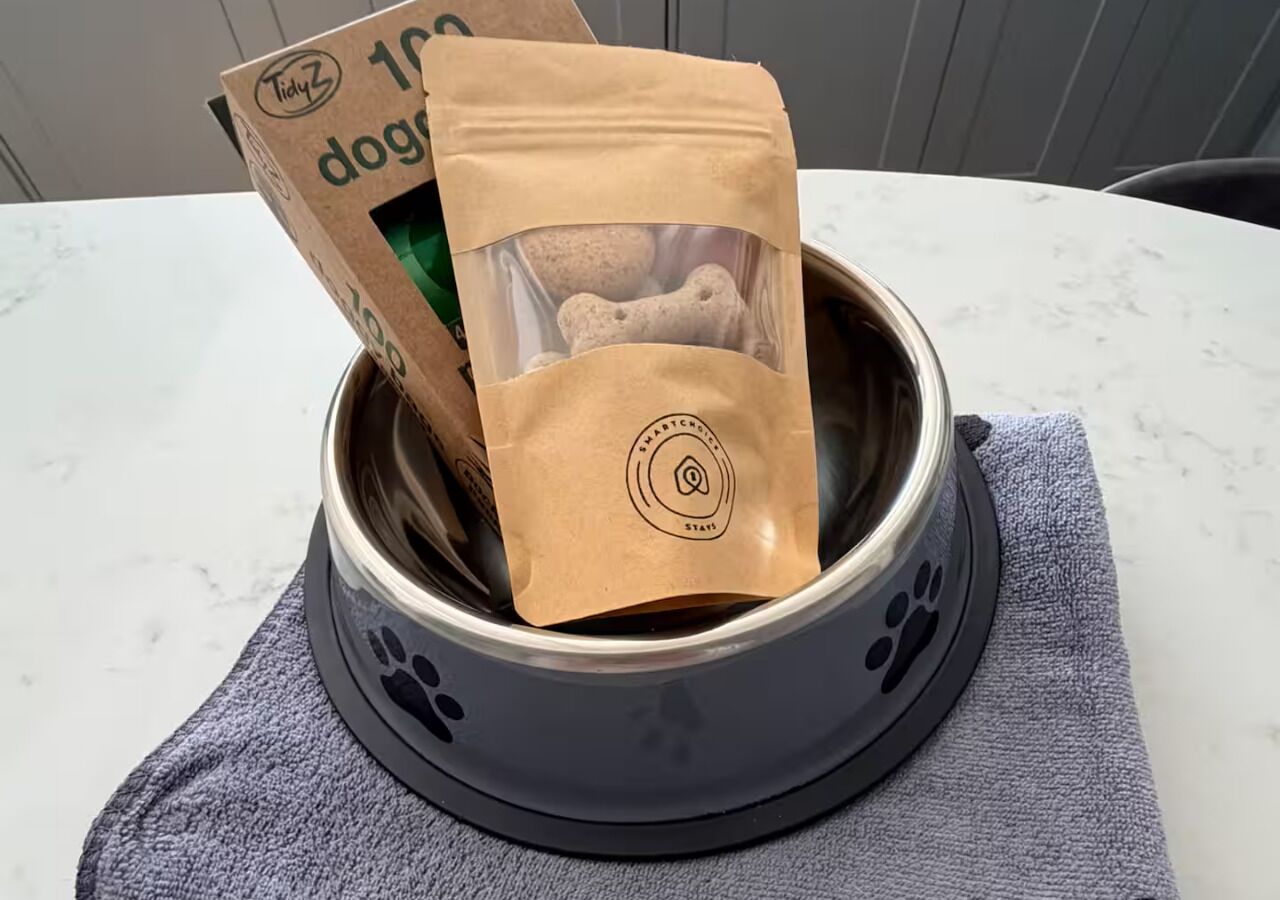 A pet bowl with a brown paper bag containing dog food, placed on a gray towel.