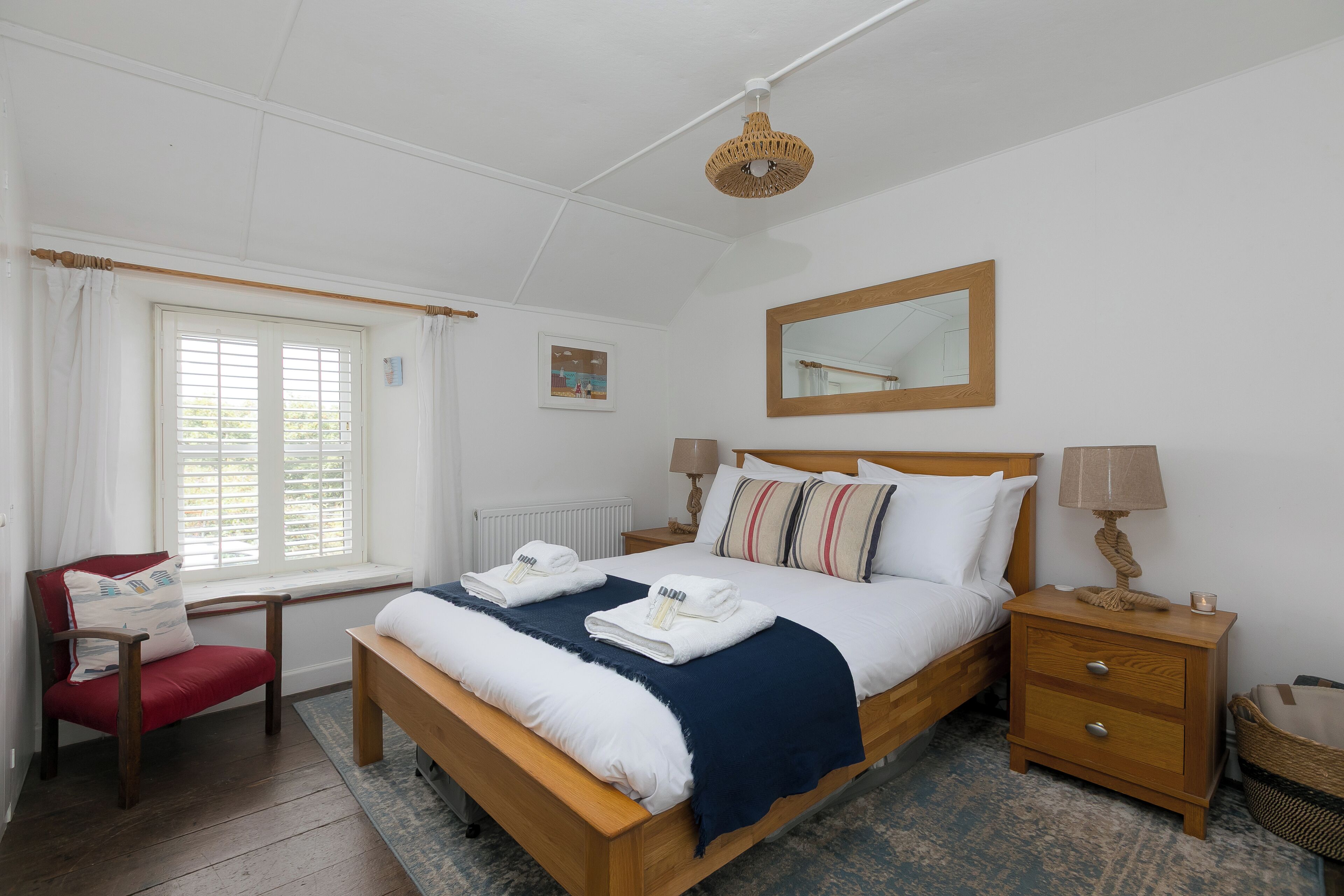 Een goed verlichte slaapkamer met een bed, nachtkastjes, een stoel, een raam met gordijnen en een hanglamp.
