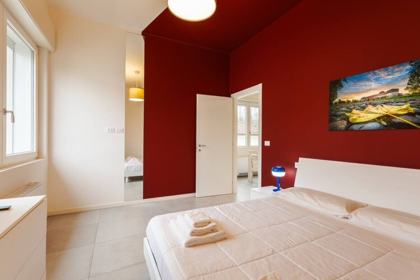 Un dormitorio con cama, escritorio, silla, un cuadro y una puerta que da a otra habitación.