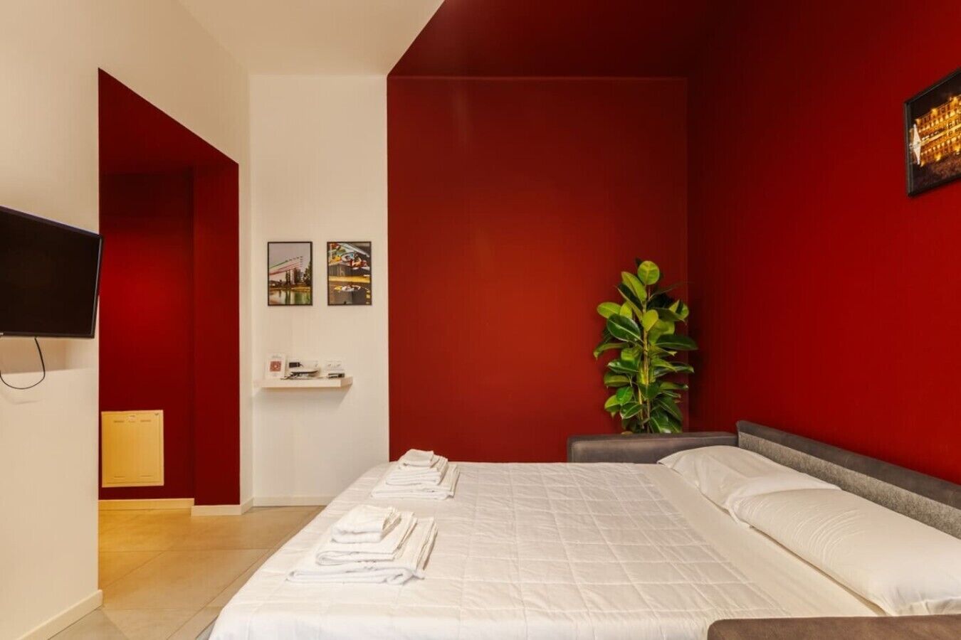 Habitación de hotel con cama, televisor, planta y pared decorada en rojo.