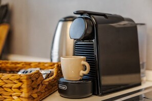 Eine Kaffeemaschine mit einer Tasse auf einem Tablett, ein gewebter Korb und ein Behälter mit Logo.