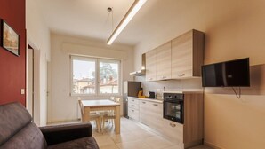 A modern kitchen with wooden cabinets, a dining table, and a TV mounted on the wall. - Tosa Apt - 500m from the Racetrack - Free WiFi & Parking (Imola)