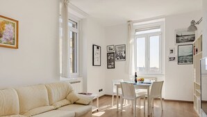 En stue med en beige sofa, et spisebord med stole og et vindue med gardiner.