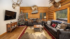 L’intérieur d’une cabane en rondins, avec une cheminée, un sapin de Noël et des têtes d’animaux empaillées accrochées aux murs.