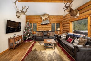 Ein Holzblockhaus-Interieur mit Kamin, Weihnachtsbaum und aufgehängten Tierköpfen.