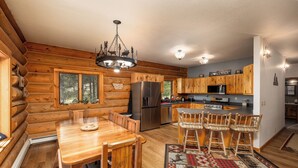 L’intérieur d’une cabane en rondins, avec une table à manger en bois, des chaises, un lustre, un réfrigérateur et un coin cuisine.