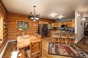 Ein rustikales Holzhaus-Interieur mit einem Holzesstisch, Stühlen, einer Deckenleuchte, einem Kühlschrank und einer Küchenzeile.