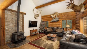 L’intérieur d’une cabane en rondins, avec une cheminée en pierre, un plafond en bois, un canapé en cuir et des têtes d’animaux empaillées accrochées au mur.