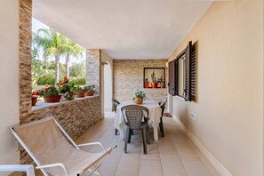 Eine überdachte Terrasse im Freien mit Tisch und Stühlen, Topfpflanzen und Blick auf Grün.