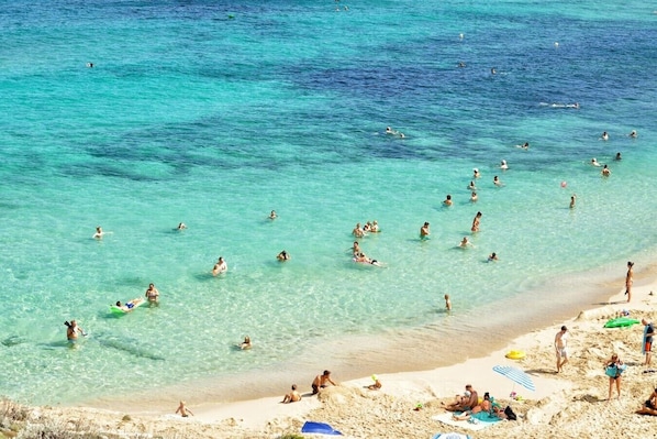 A beach with clear turquoise water, people swimming and sunbathing, and a sandy shore with umbrellas and beach chairs. - Family Vacation in a Villa with Bikes and a Terrace (Ognina)