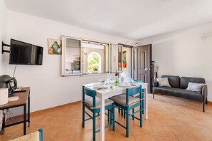 A dining area with a table and chairs, a television mounted on the wall, and a sofa in the background. - Family Vacation in a Villa with Bikes and a Terrace (Ognina)