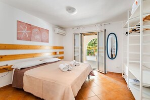 A bedroom with a wooden headboard, a bed with a beige blanket, a white air conditioner, a sliding glass door to a balcony, and a white shelving unit. - Family Vacation in a Villa with Bikes and a Terrace (Ognina)