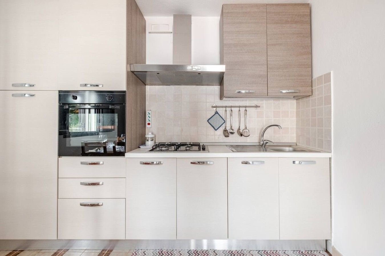 A modern kitchen with white cabinetry, a built-in oven, a gas stove, and a stainless steel range hood.