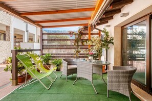 Eine Terrasse im Freien mit Korbmöbeln, grünen Stühlen und Topfpflanzen.