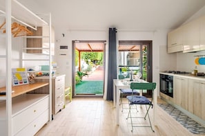A modern kitchen with a dining area, a small seating space, and a view of a garden. - Studio in a Villa · Private Veranda · 200m from the Sea (Ognina)