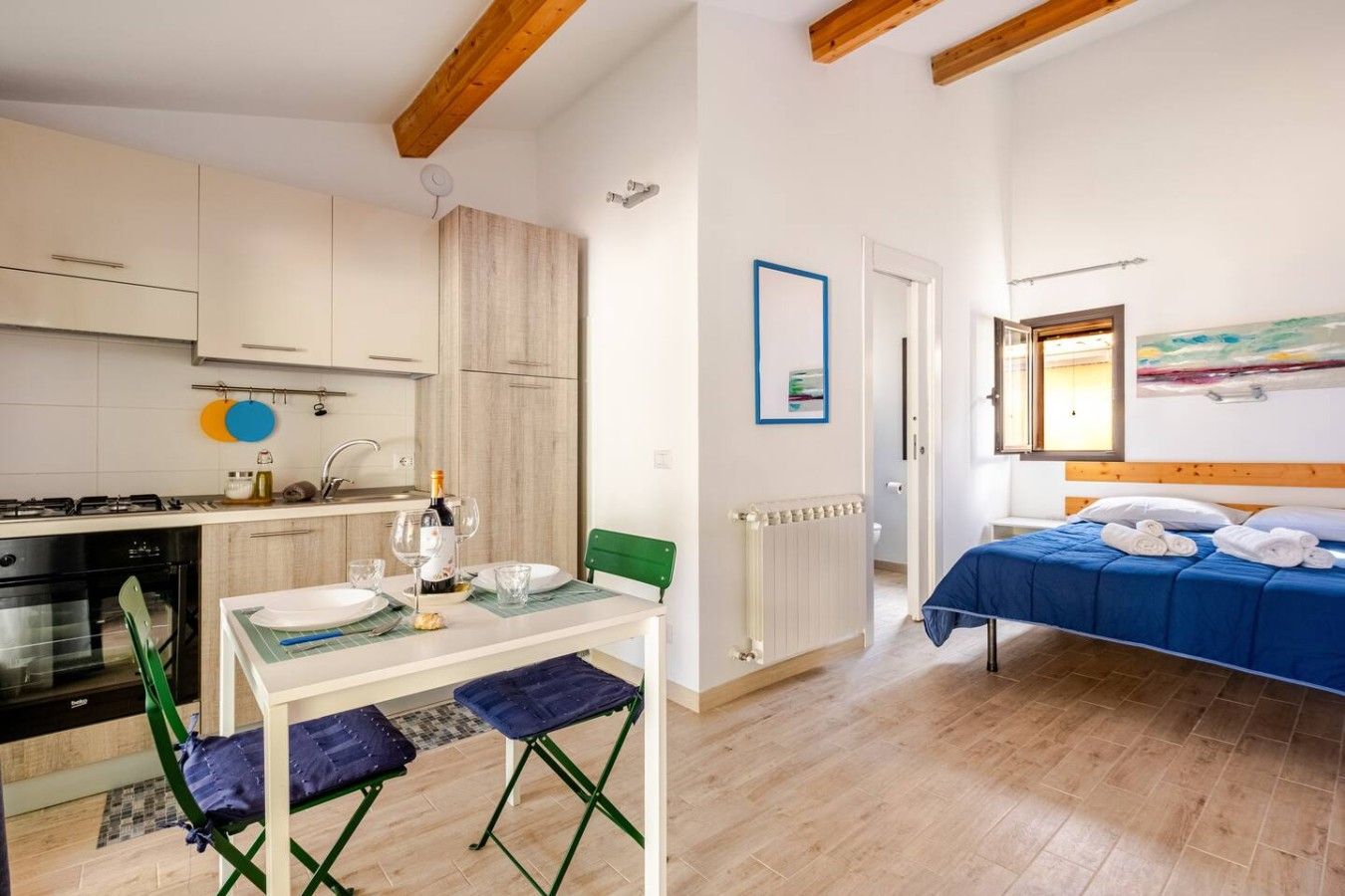 Een compacte kamer met een kitchenette, een eethoek met een tafel en stoelen, en een bed met een blauw dekbed.