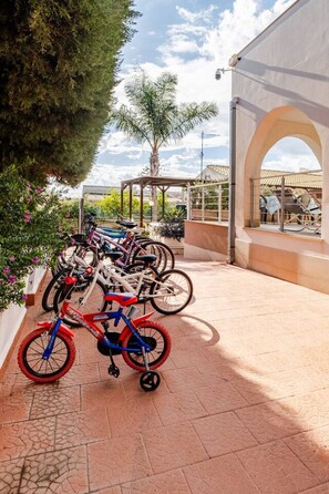 Un espacio exterior pavimentado con una fila de bicicletas estacionadas bajo una estructura cubierta.