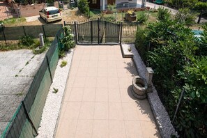 Un vialetto lastricato conduce a un cancello, circondato da vegetazione e da una recinzione.