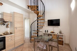 Uma cozinha compacta com armários de madeira, uma mesa de jantar de vidro, uma escada em espiral e uma televisão de tela plana.