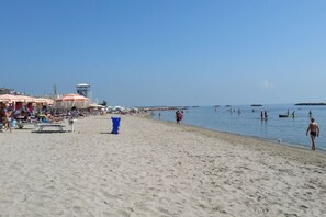 Uma praia com guarda-sóis, espreguiçadeiras e uma torre de salva-vidas.