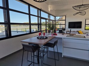 A modern kitchen with a large window, a dining area with two chairs, a table with glasses, and a plant. - Villa Locquénolé overlooking Morlaix Bay (Locquénolé)