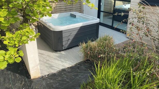 Een bubbelbad in een moderne buitenomgeving, met een glazen deur en een betonnen vloer.