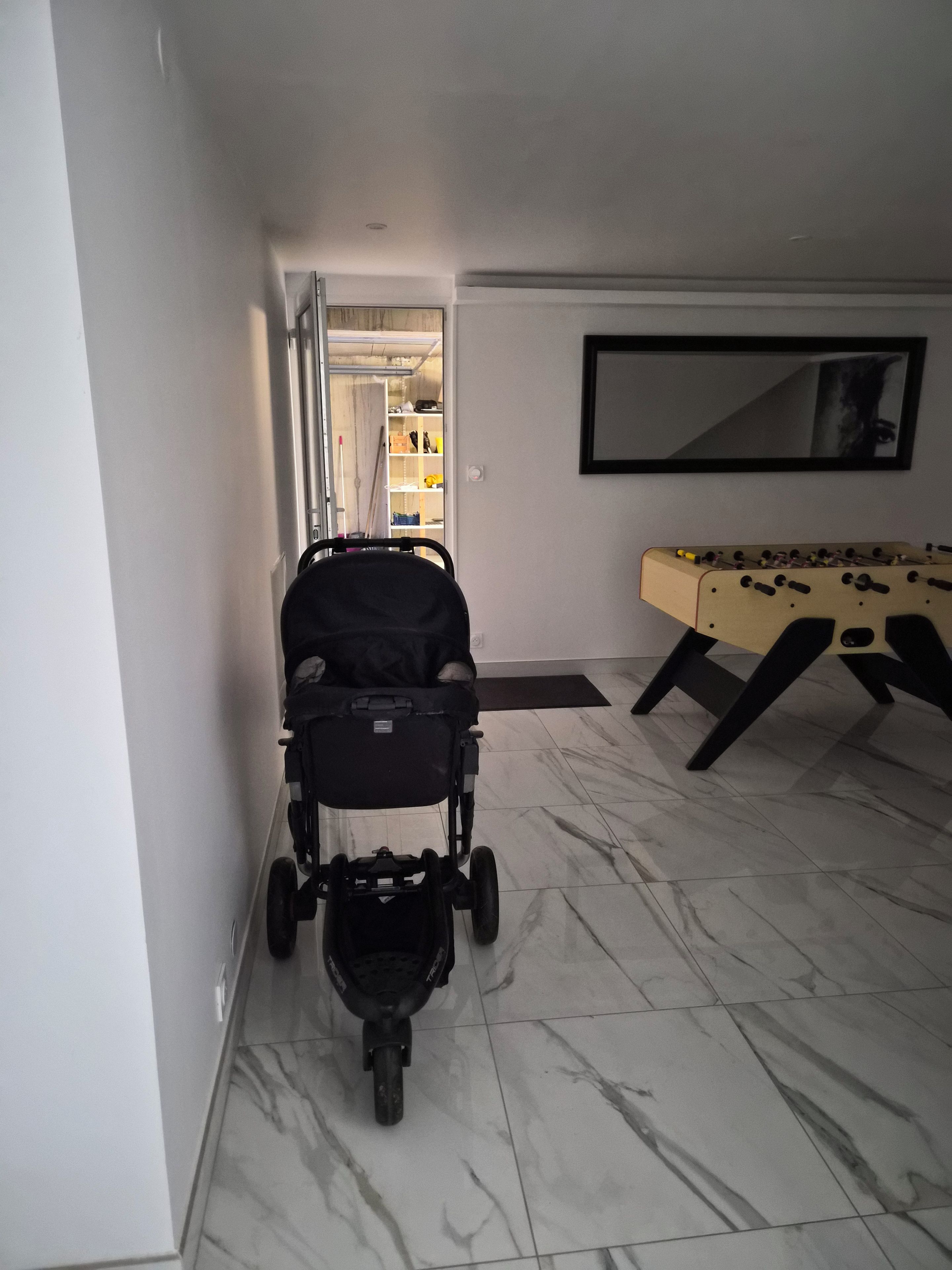 Ein Zimmer mit Kinderwagen, Kicker und einer Tür zu einem Lagerraum.