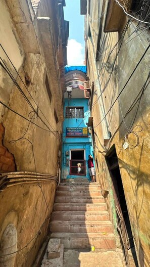 Um beco estreito com uma escadaria que leva a um edifício de fachada azul e uma placa.