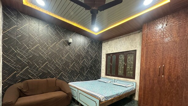 A bedroom with a bed, a brown sofa, a wardrobe, and a ceiling fan.