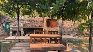 Un espacio de estar al aire libre rústico con pared de piedra, mesa y bancos de madera, y una pérgola con parras.
