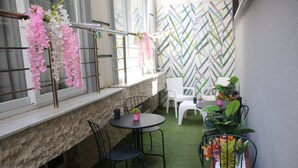 Un espace patio agrémenté d’un mur en pierre, d’une fenêtre ornée de fleurs roses et blanches, d’une chaise en métal, d’une table ronde et d’une plante en pot.