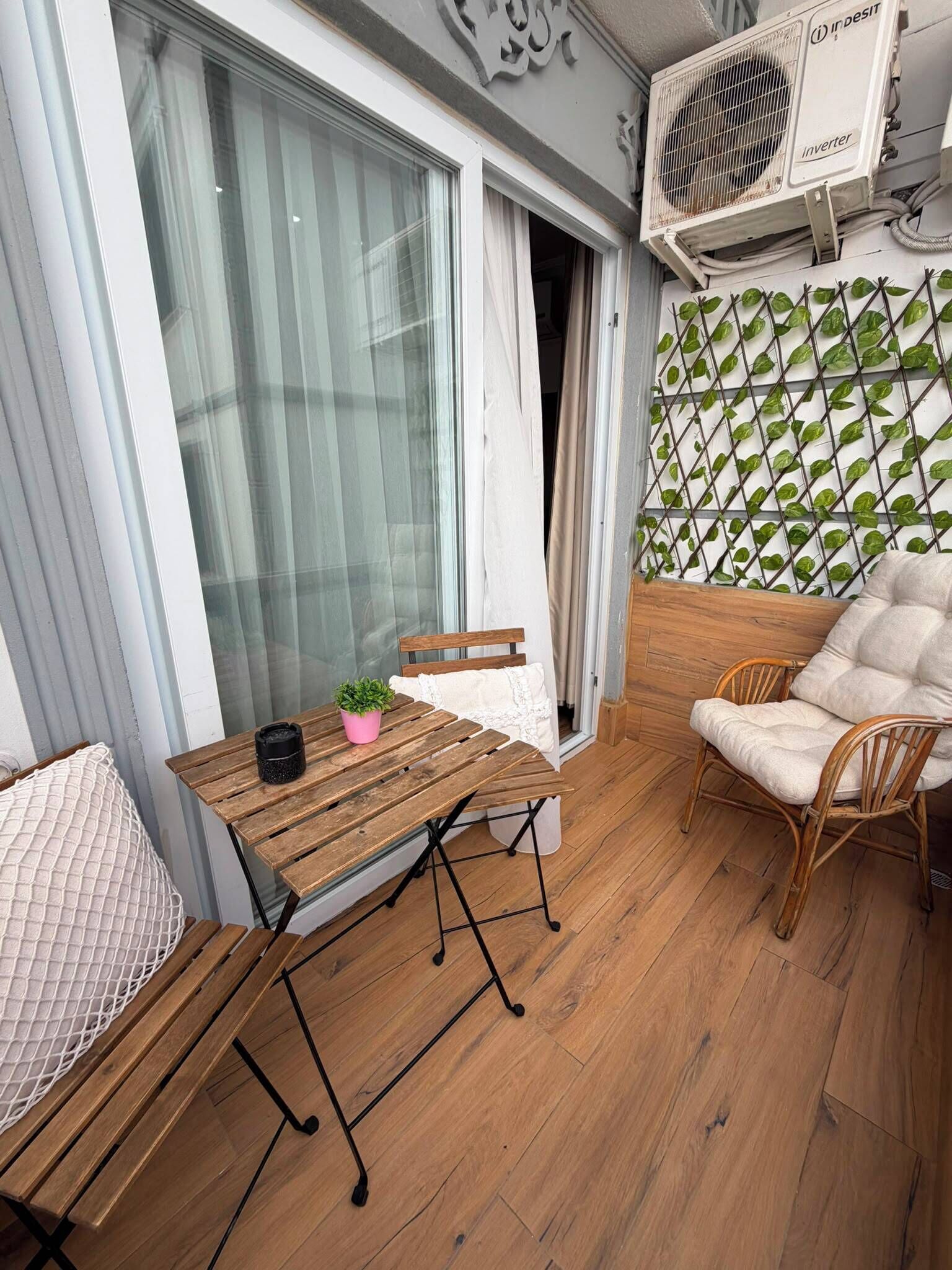 Un balcon avec une table en bois, une chaise en osier, un pot de fleurs et un coussin blanc.